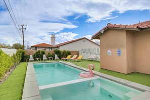 A swimming pool with a pink flamingo float, surrounded by green artificial grass and white lounge chairs. - Desert Hot Springs Home w/ Pool & Gas Grill! (Desert Hot Springs)