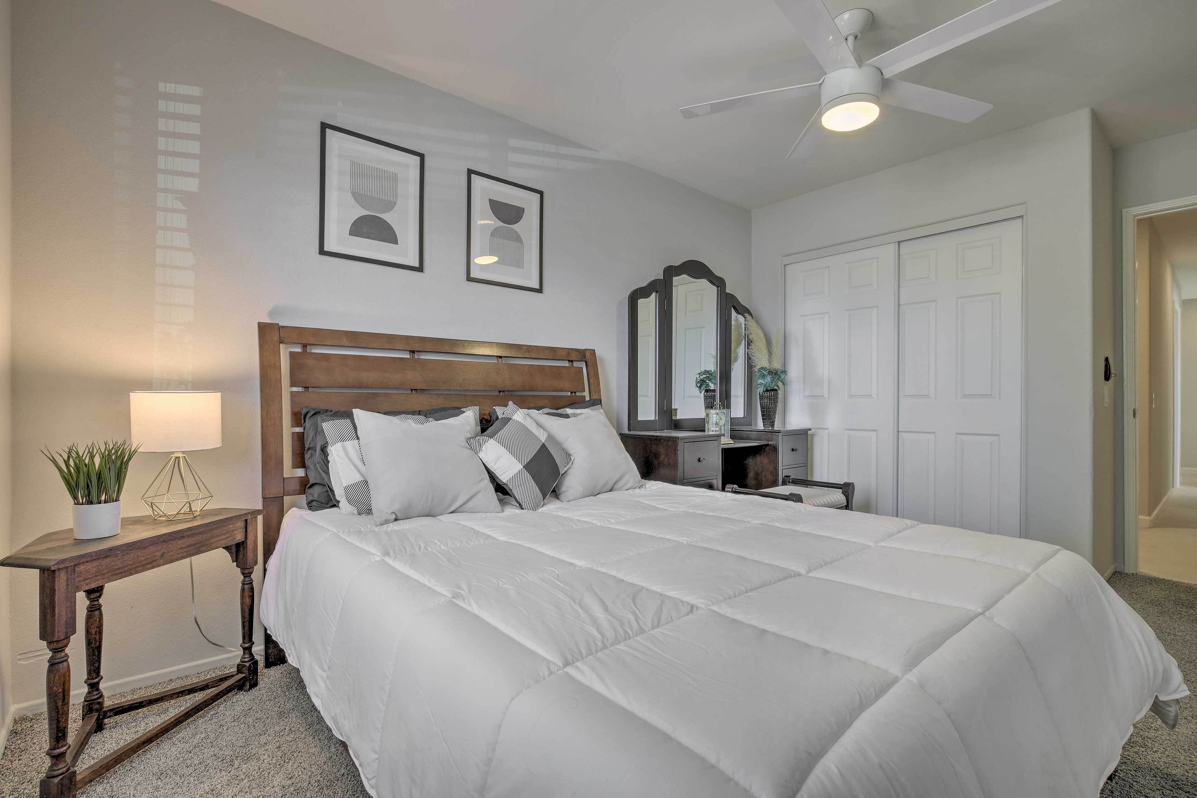 A bedroom with a large bed, a wooden nightstand, a mirror, and a ceiling fan.