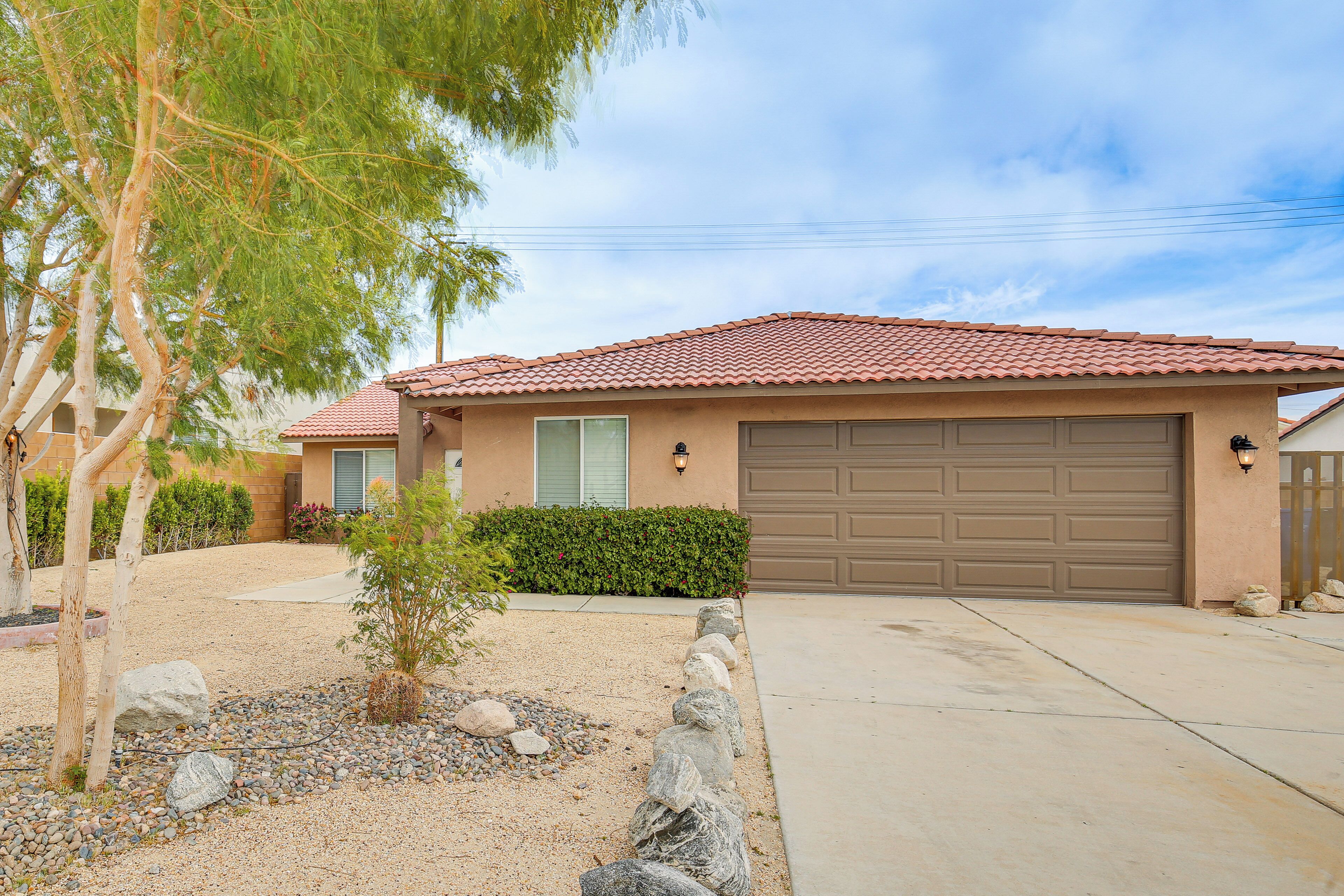 A single-story house with a red-tiled roof, a garage, and a landscaped front yard with rocks and a small tree.