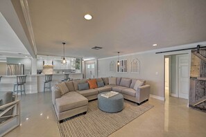 A spacious living area with a large L-shaped sectional sofa, a round ottoman, and a kitchen in the background.