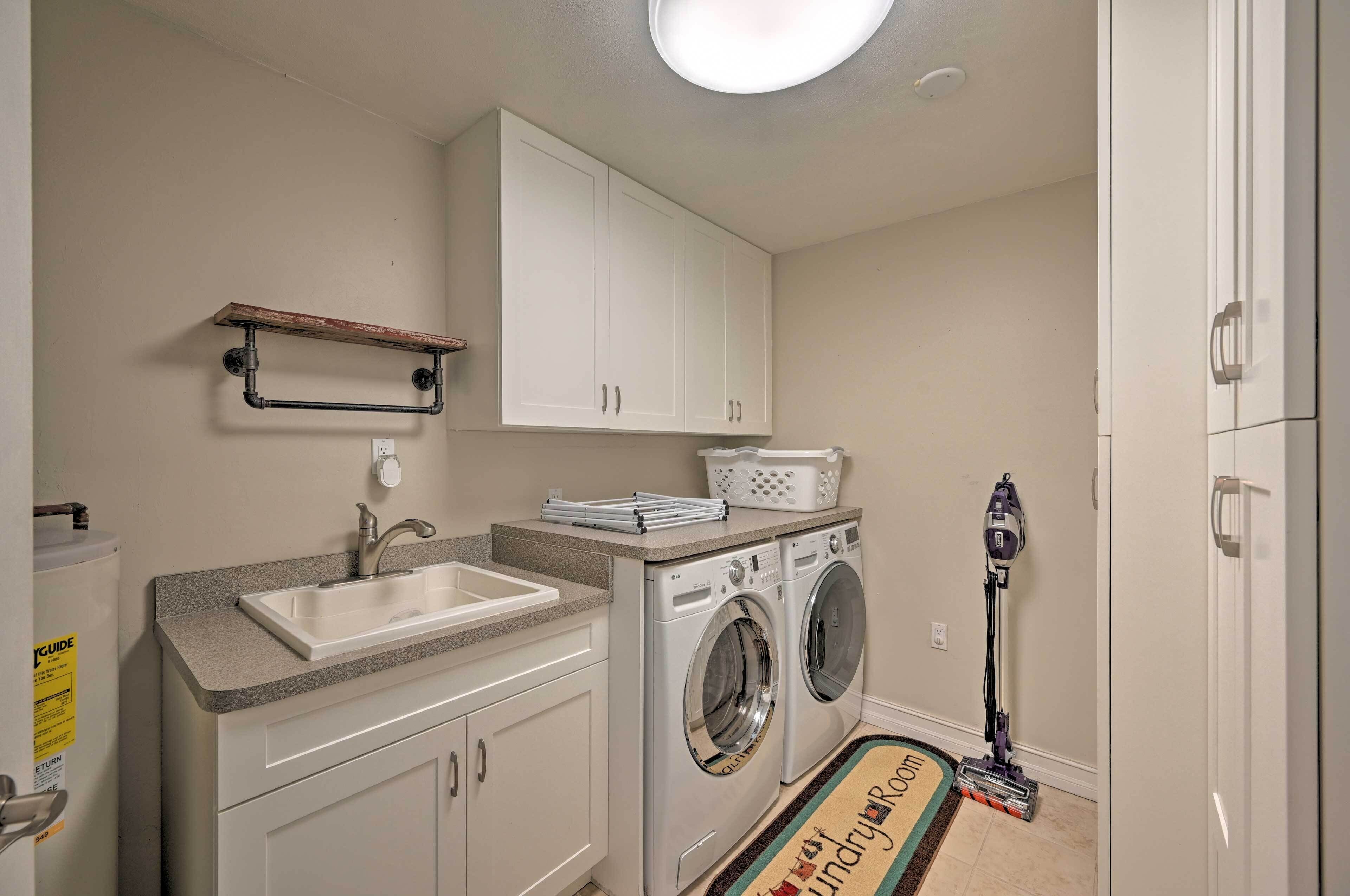 A laundry room with a washing machine, dryer, sink, and a vacuum cleaner.
