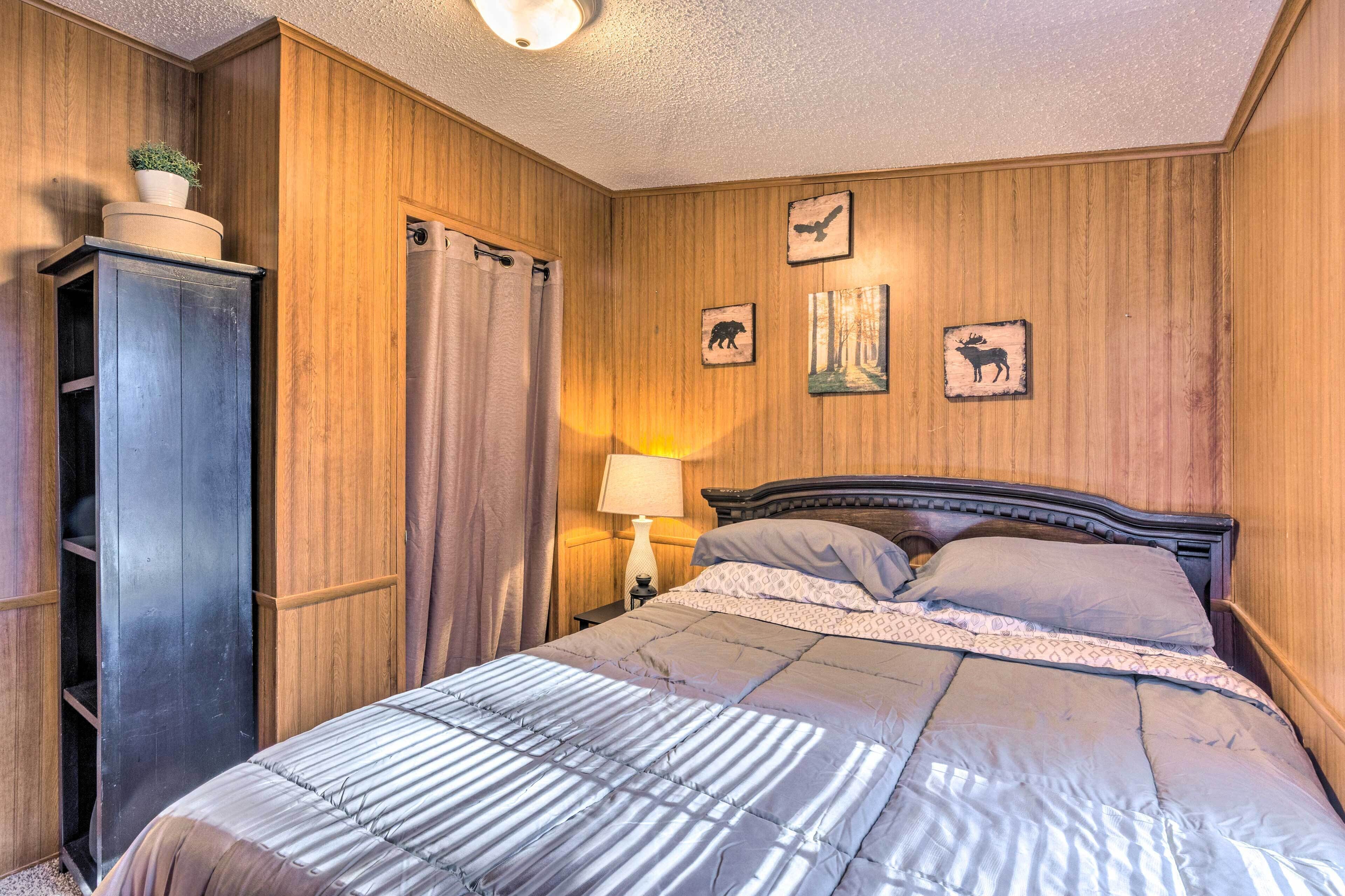 A bedroom with a wooden paneled wall, a bed with a striped comforter, a nightstand with a lamp, and a wardrobe.