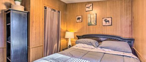 A bedroom with a wooden paneled wall, a bed with a striped comforter, a nightstand with a lamp, and a wardrobe.