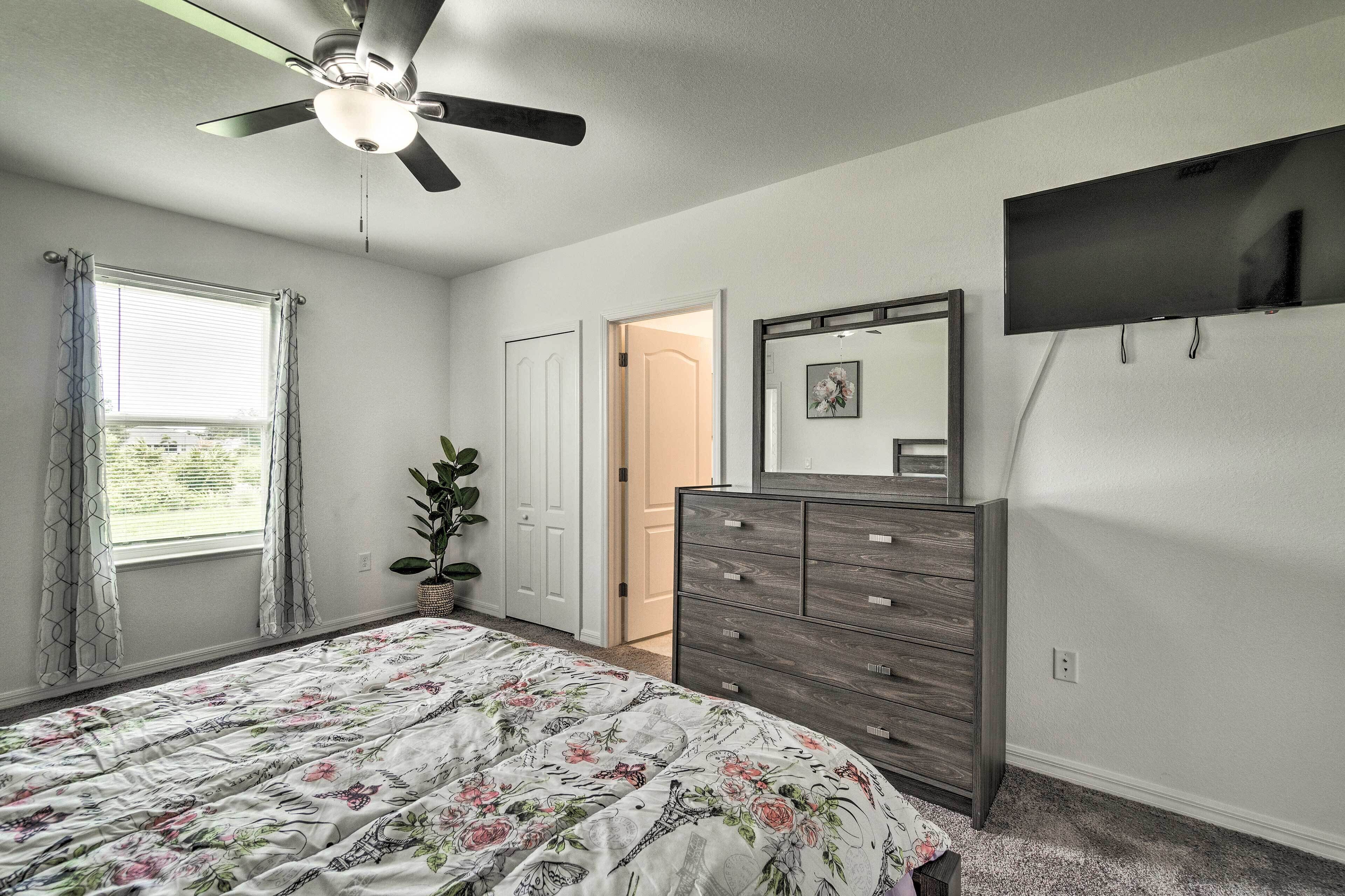 A bedroom with a bed, a dresser, a ceiling fan, a TV, and a window with curtains.