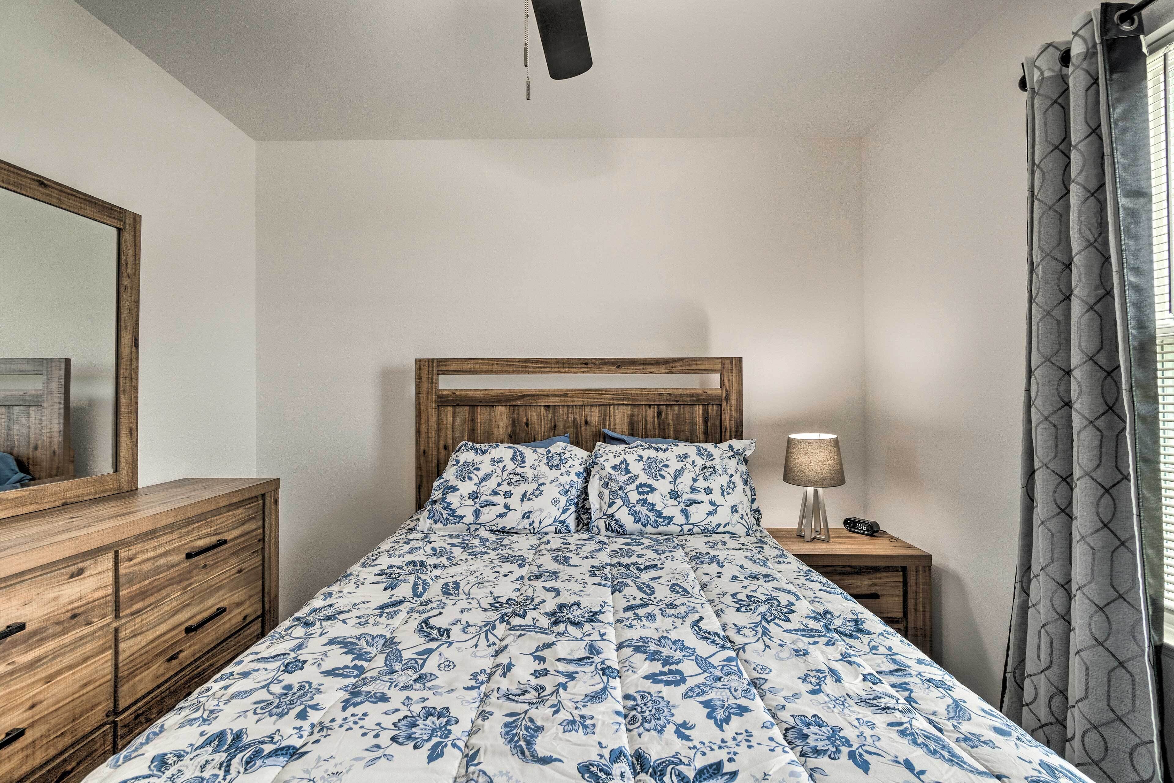 Una camera da letto con una testiera in legno, un letto con lenzuola a motivi floreali, un comodino con una lampada e uno specchio appeso al muro.