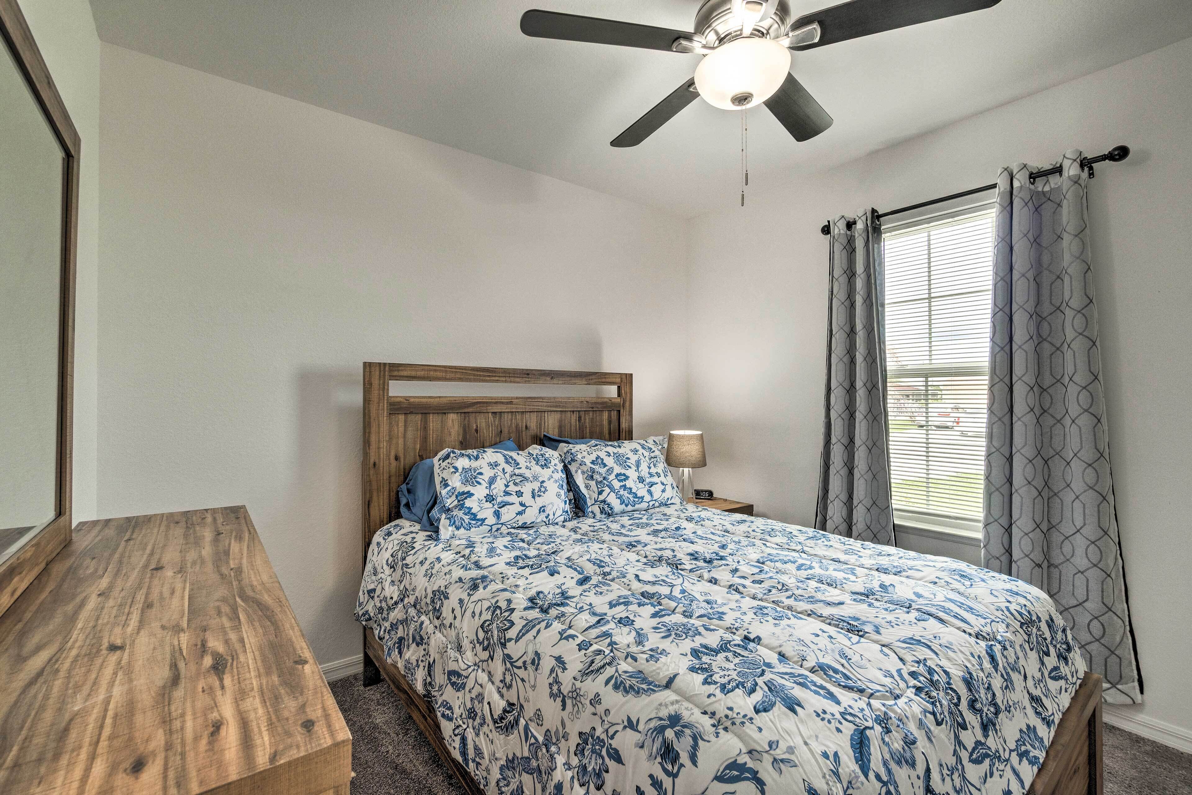 A bedroom with a wooden bed, a nightstand, a ceiling fan, and a window with curtains.