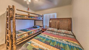A room with bunk beds, a ceiling fan, a window with blinds, and a wooden headboard.