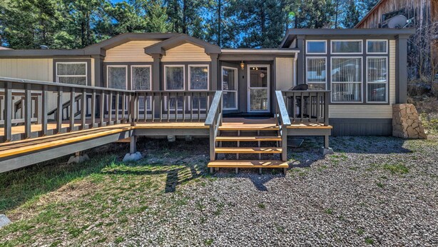 A two-story cabin with a wooden deck, a front porch, and a stone wall.