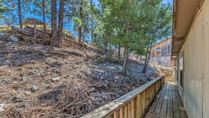A wooden deck leading to a building with a view of a rocky hillside and trees.