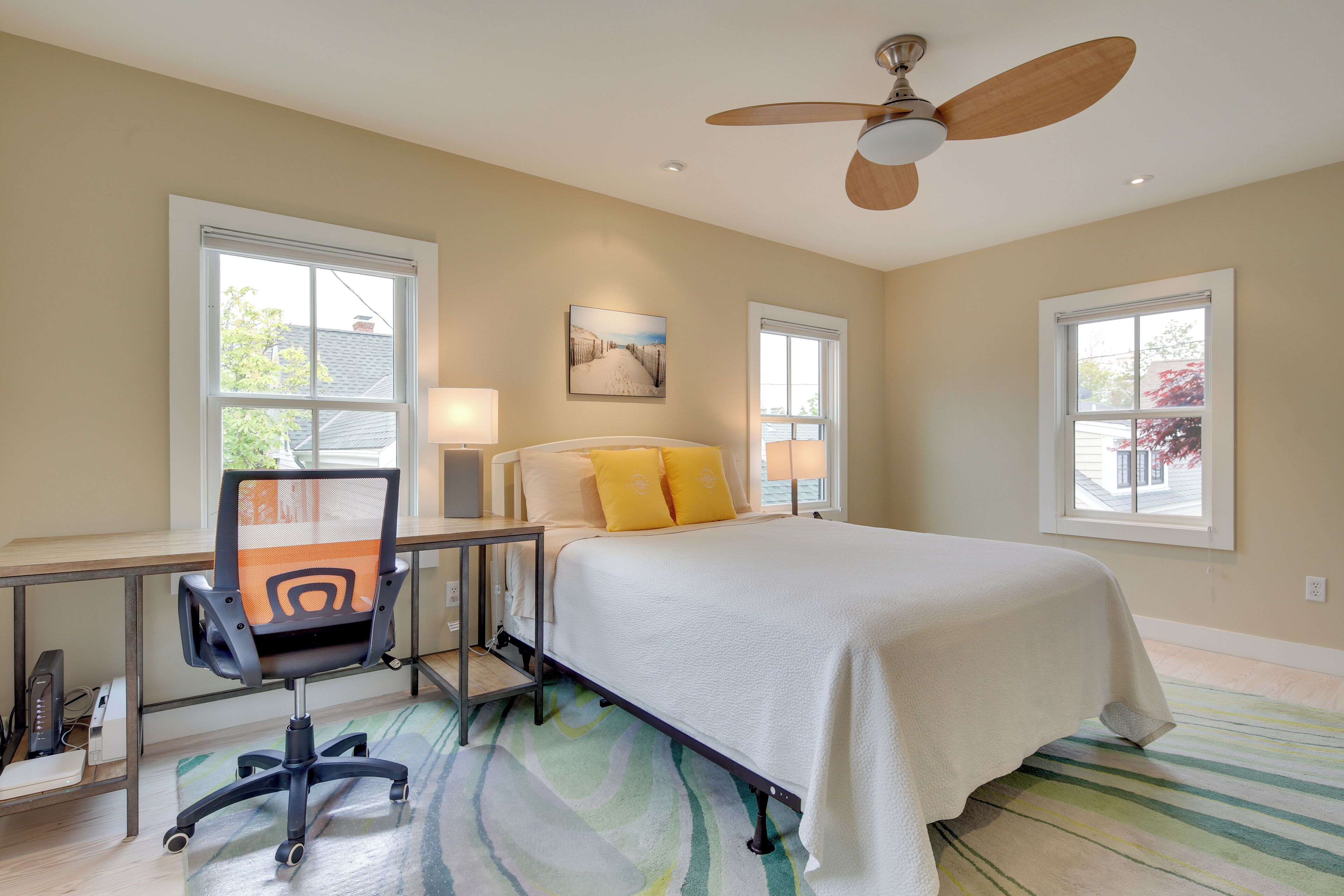 A bedroom with a bed, desk, chair, and ceiling fan.