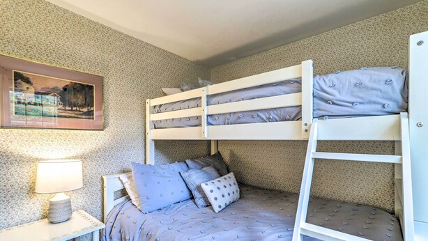 A bunk bed with a patterned bedspread, a bedside table with a lamp, and a framed picture on the wall. - Yarmouth Cottage w/ Grill & Yard, Walk to Beach (West Yarmouth)