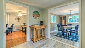 A dining area with a wooden table and chairs, a clock on the wall, and an American flag. - Yarmouth Cottage w/ Grill & Yard, Walk to Beach (West Yarmouth)