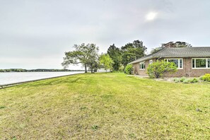 A house with a grassy lawn and a view of a lake. - Bayfront Retreat w/ Game Room + Outdoor Pool! (Exmore)