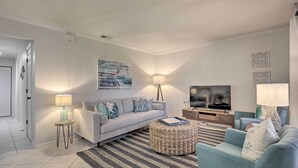 A modern living room with a sofa, ottoman, and TV. - Sunny St Augustine Condo w/ Wifi - Walk to Beach! (St. Augustine)