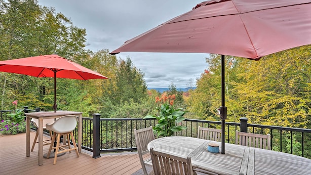 A wooden deck with a table and chairs, two red umbrellas, and a view of autumn trees. - Cozy Home w/ Sauna: Mins to Stowe Mountain Resort (Stowe)