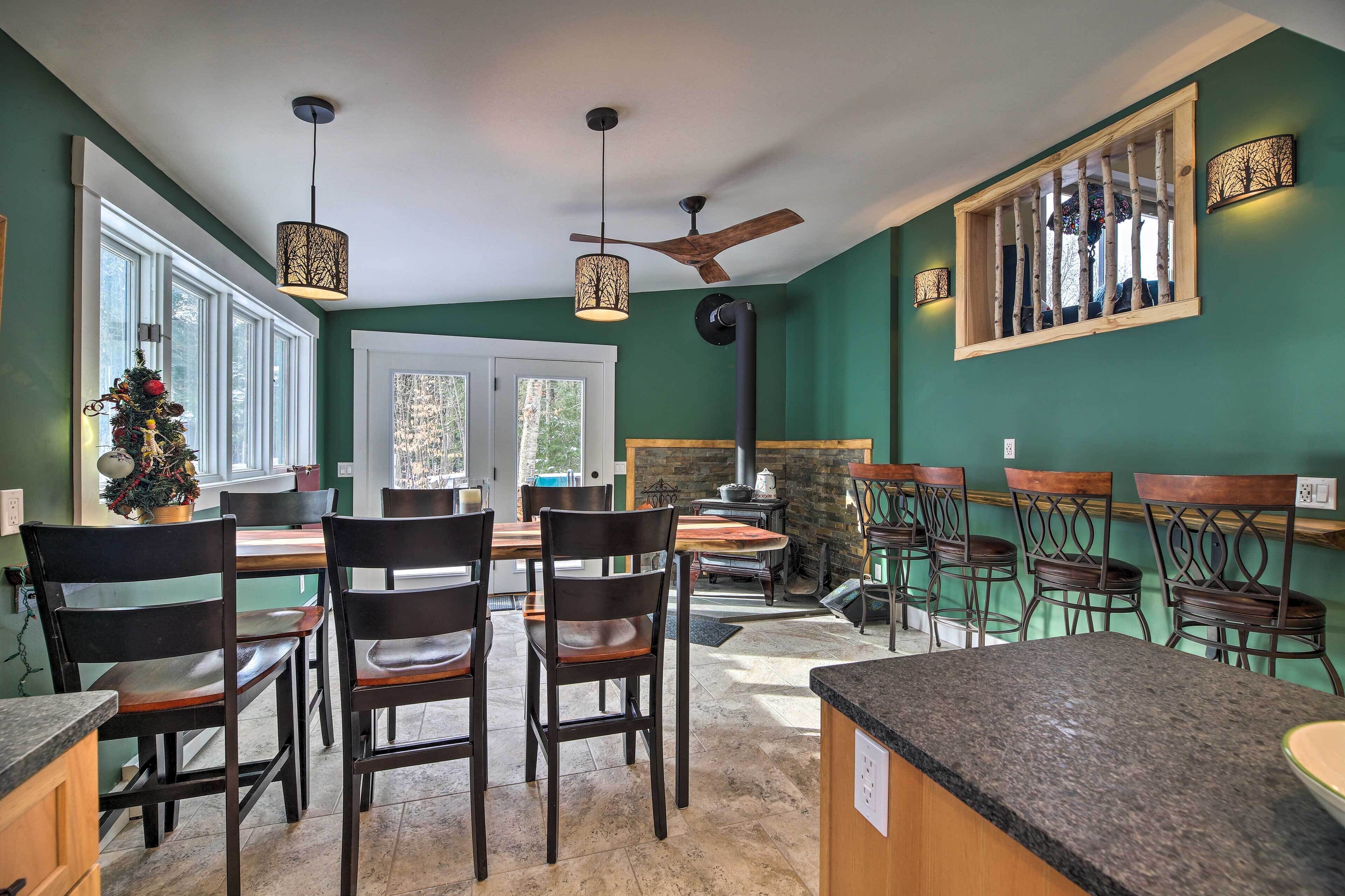 Un coin repas avec des chaises et des tables en bois, un ventilateur de plafond et une fenêtre donnant sur les arbres.