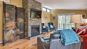A living room with a stone fireplace, a television mounted on the wall, and a seating area with two chairs and a sofa. - Cozy Home w/ Sauna: Mins to Stowe Mountain Resort (Stowe)