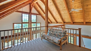 A loft bedroom with a wooden ceiling, a ceiling fan, a window, and a sofa.