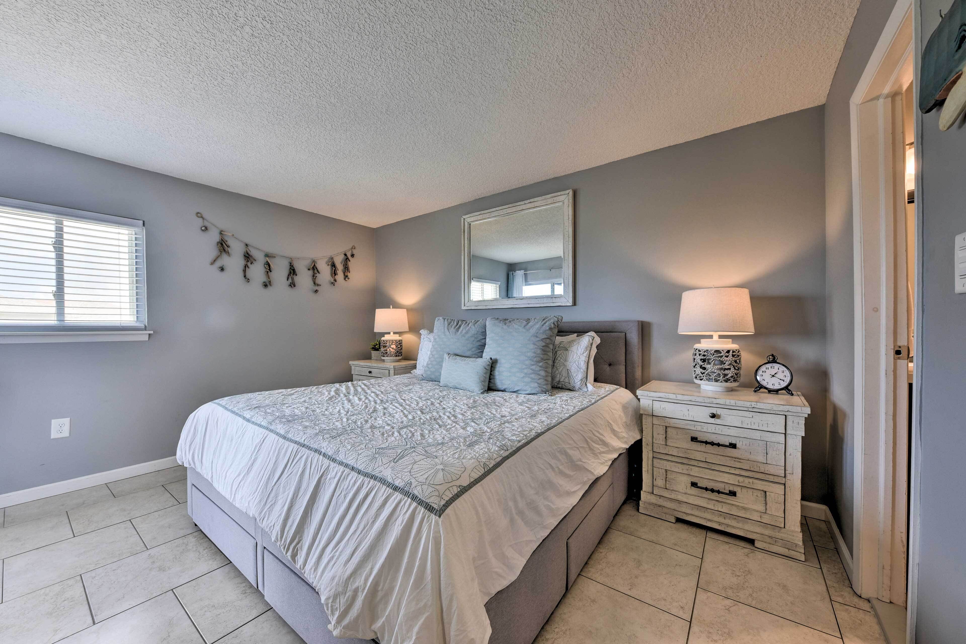 A bedroom with a bed, nightstands, a dresser, a mirror, and a window with blinds.