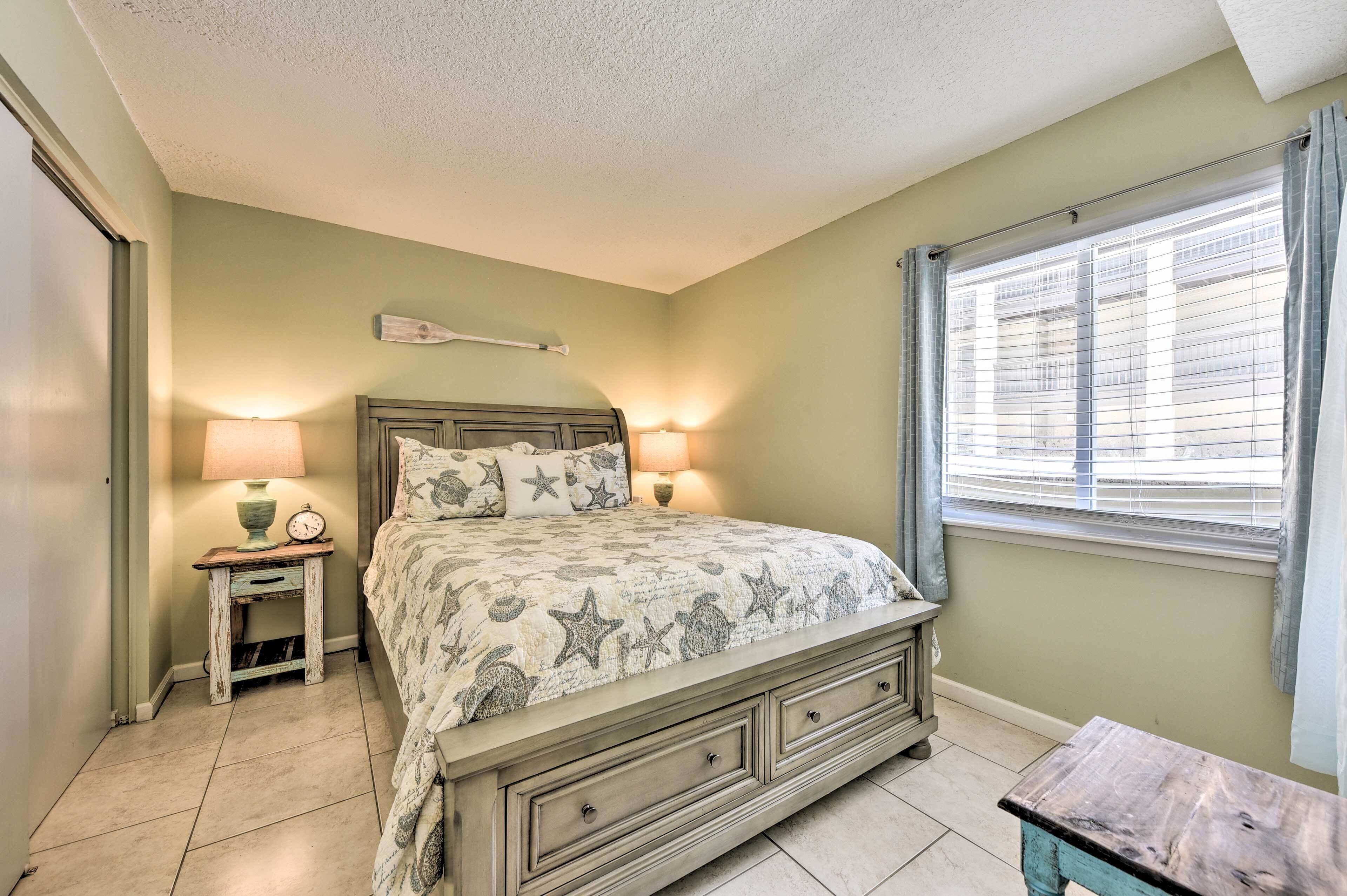 A bedroom with a bed, bedside lamps, a small table, and a window with blinds.