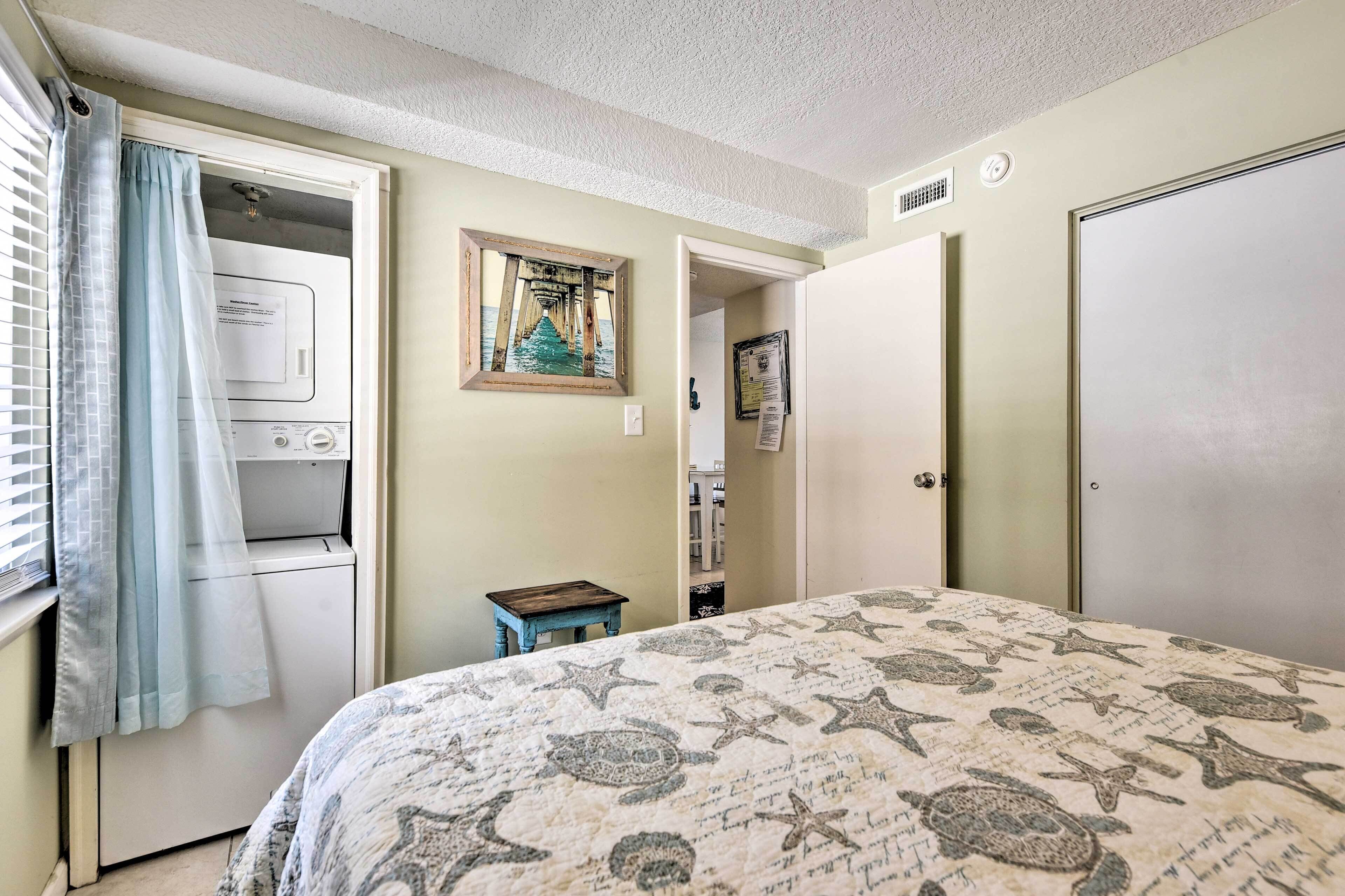 Une chambre à coucher comprenant un lit, un lave-linge, une petite table et une porte donnant sur une autre pièce.