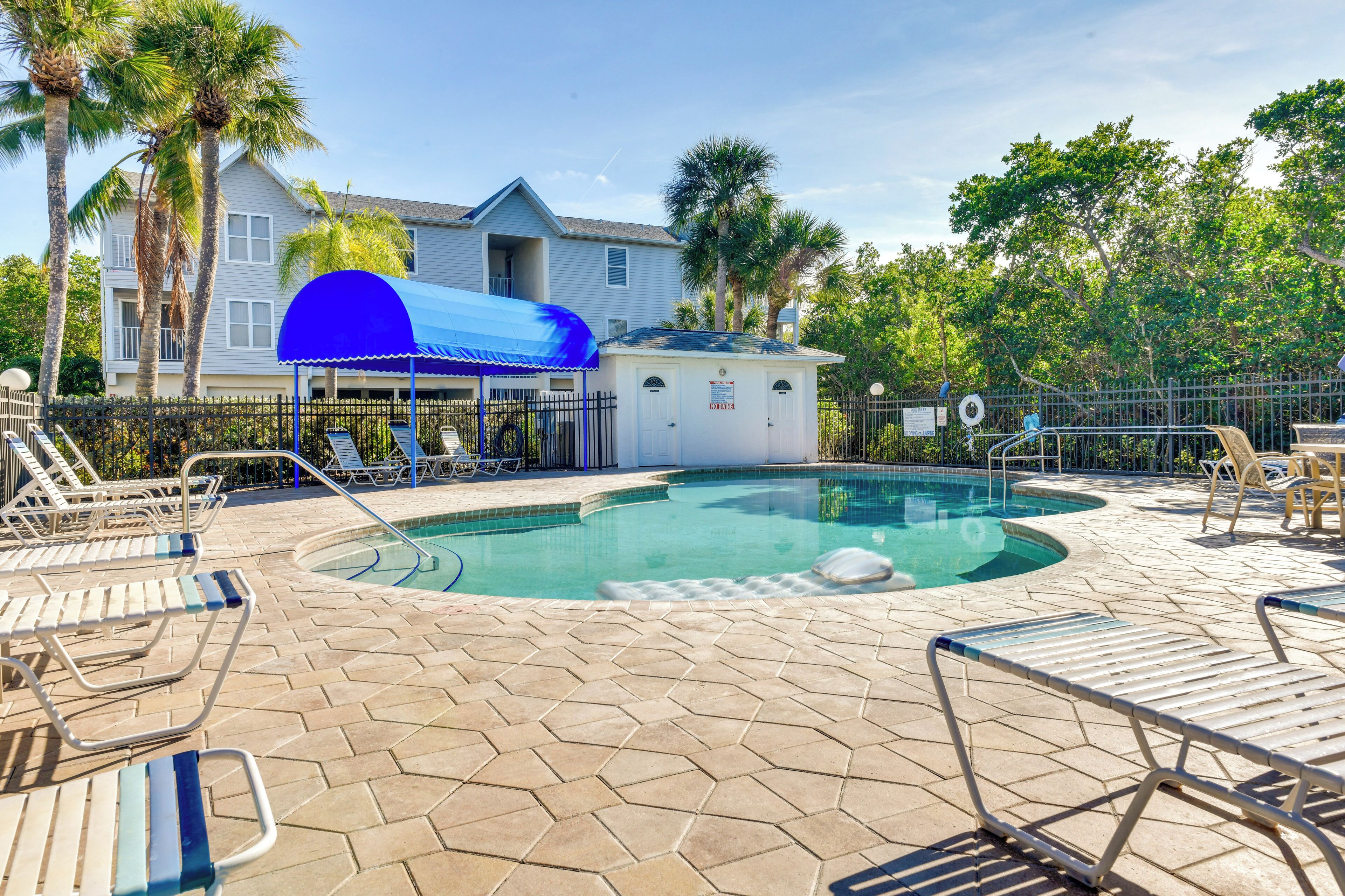 A swimming pool with lounge chairs, a covered area, and a house in the background.