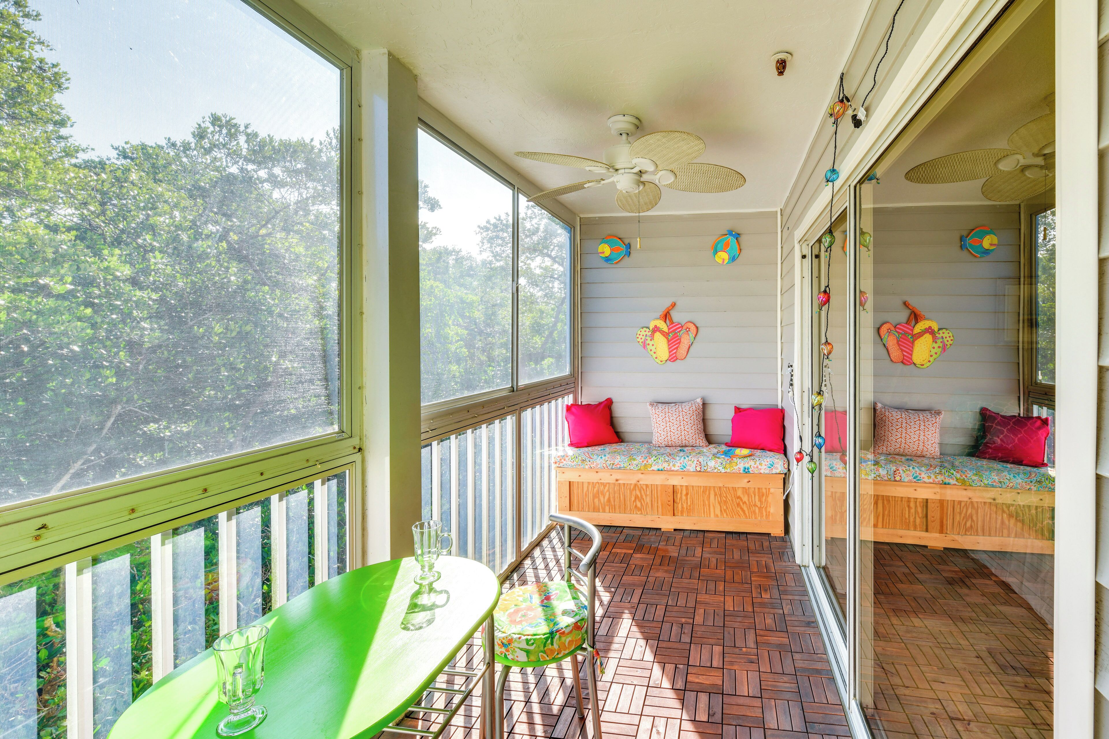 Un balcon avec une table et des chaises, un ventilateur de plafond et un lit agrémenté de coussins colorés.