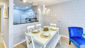 A modern dining area with a glass table, white chairs, and a blue velvet chair. - Walk to Beach: Home w/ Porch on Anna Maria Island! (Holmes Beach)