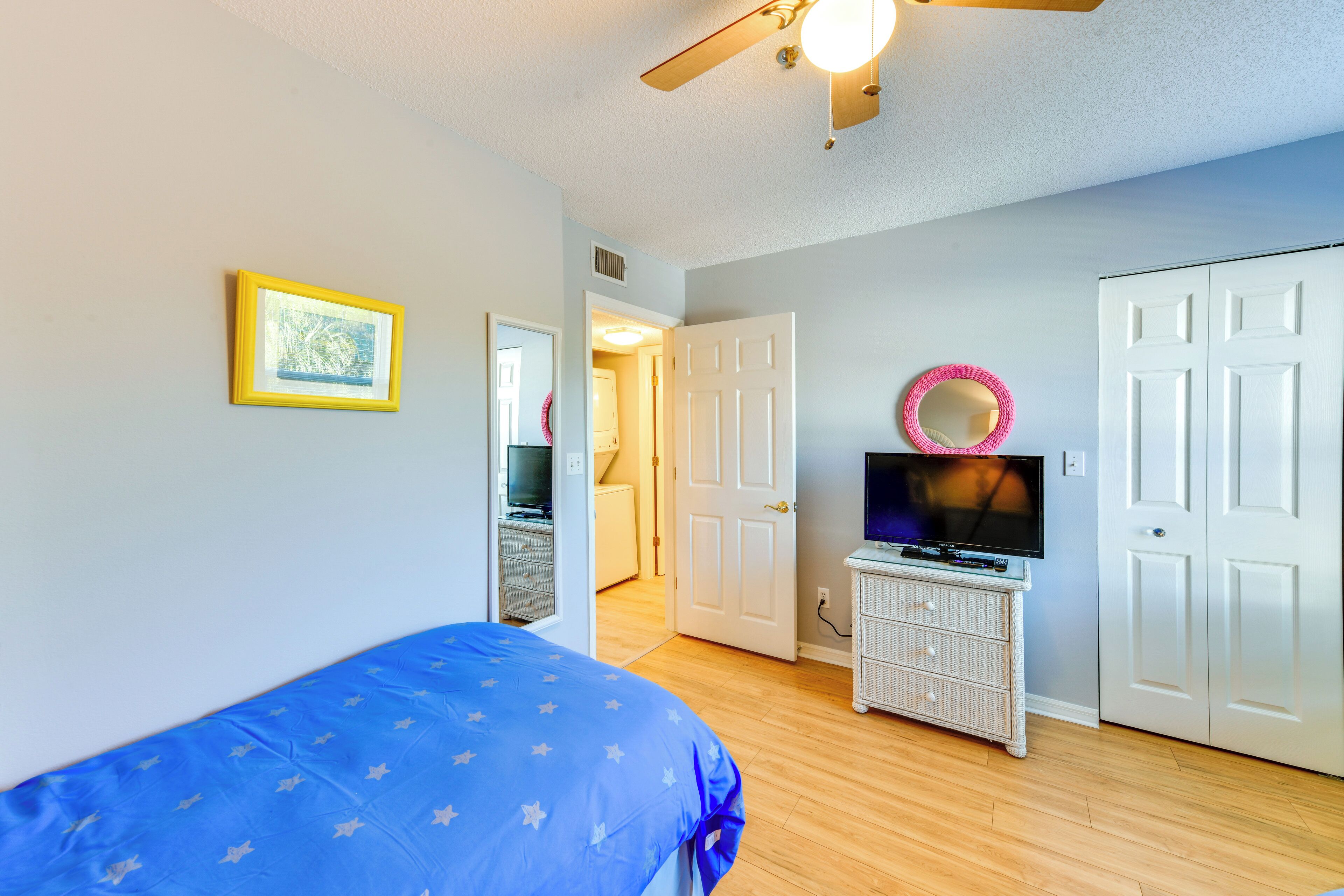 A bedroom with a bed, a television on a dresser, a door, and a ceiling fan.