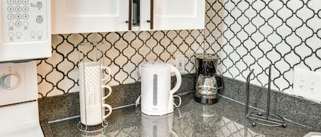 Et køkken med en hvid kaffemaskine, elkedel og kaffekande på en granitbordplade.