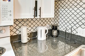 Una cocina con cafetera blanca, hervidor y jarra para café sobre una encimera de granito.