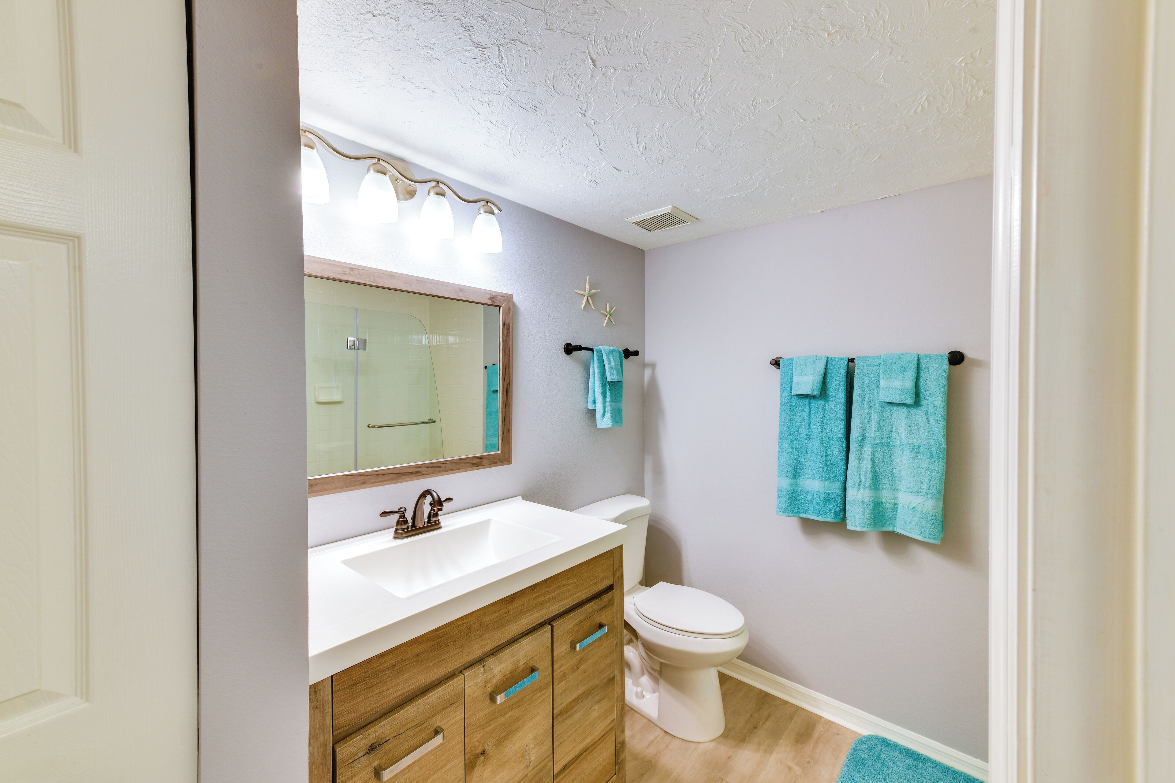 A bathroom with a white sink, wooden vanity, and a toilet. There are two towels hanging on hooks and a starfish decoration on the wall.