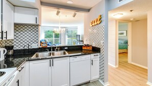 A modern kitchen with white cabinets, a black countertop, and a built-in dishwasher. - Walk to Beach: Home w/ Porch on Anna Maria Island! (Holmes Beach)