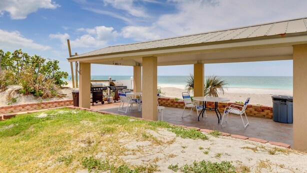 Eine Terrasse im Freien mit Grill, Sitzgelegenheiten und Blick auf den Strand.