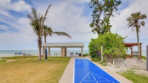 Ein Shuffleboard-Spielfeld, Strandstühle und ein Gazebo am Meer.