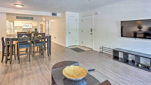 A modern living room with a dining area, a flat-screen TV mounted on the wall, and a decorative bowl on a coffee table. - Kissimmee Condo w/ Pool Access, 6 Mi to Disney! (Kissimmee)