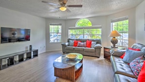 A spacious living room with a large flat-screen TV, leather sofas, a glass coffee table, and a ceiling fan. - Kissimmee Condo w/ Pool Access, 6 Mi to Disney! (Kissimmee)