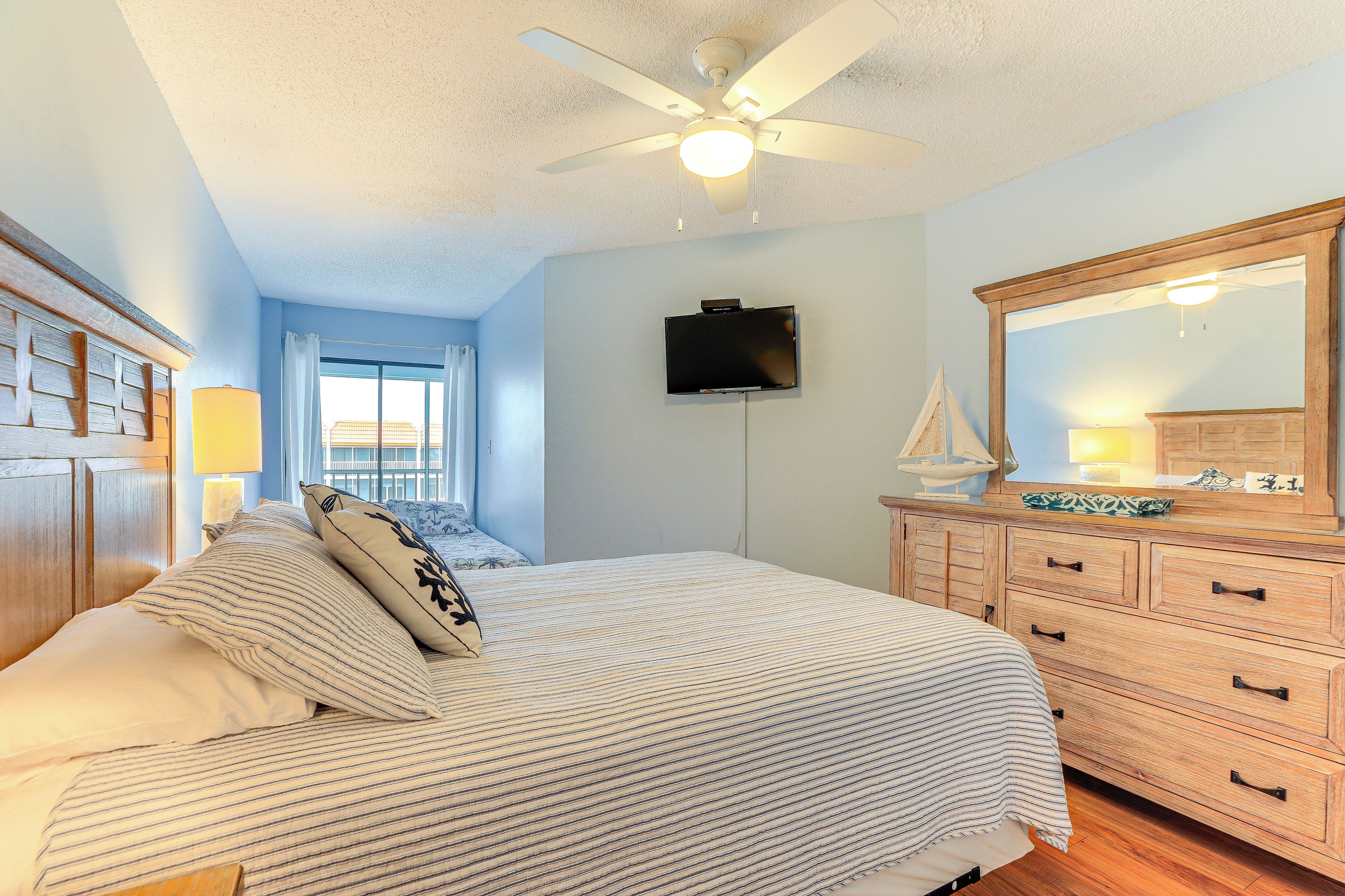 A bedroom with a bed, a dresser, a television, and a ceiling fan.