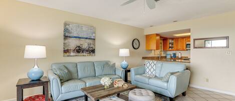 A living room with two light blue sofas, a wooden coffee table, two grey ottomans, and a patterned rug.