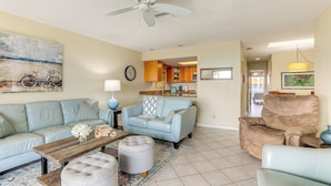 A living room with a sofa, ottoman, coffee table, and a recliner. There is a ceiling fan, a clock, and a painting on the wall. - Pelican Cove Condo at Bradenton Beach w/ Pool! (Bradenton Beach)