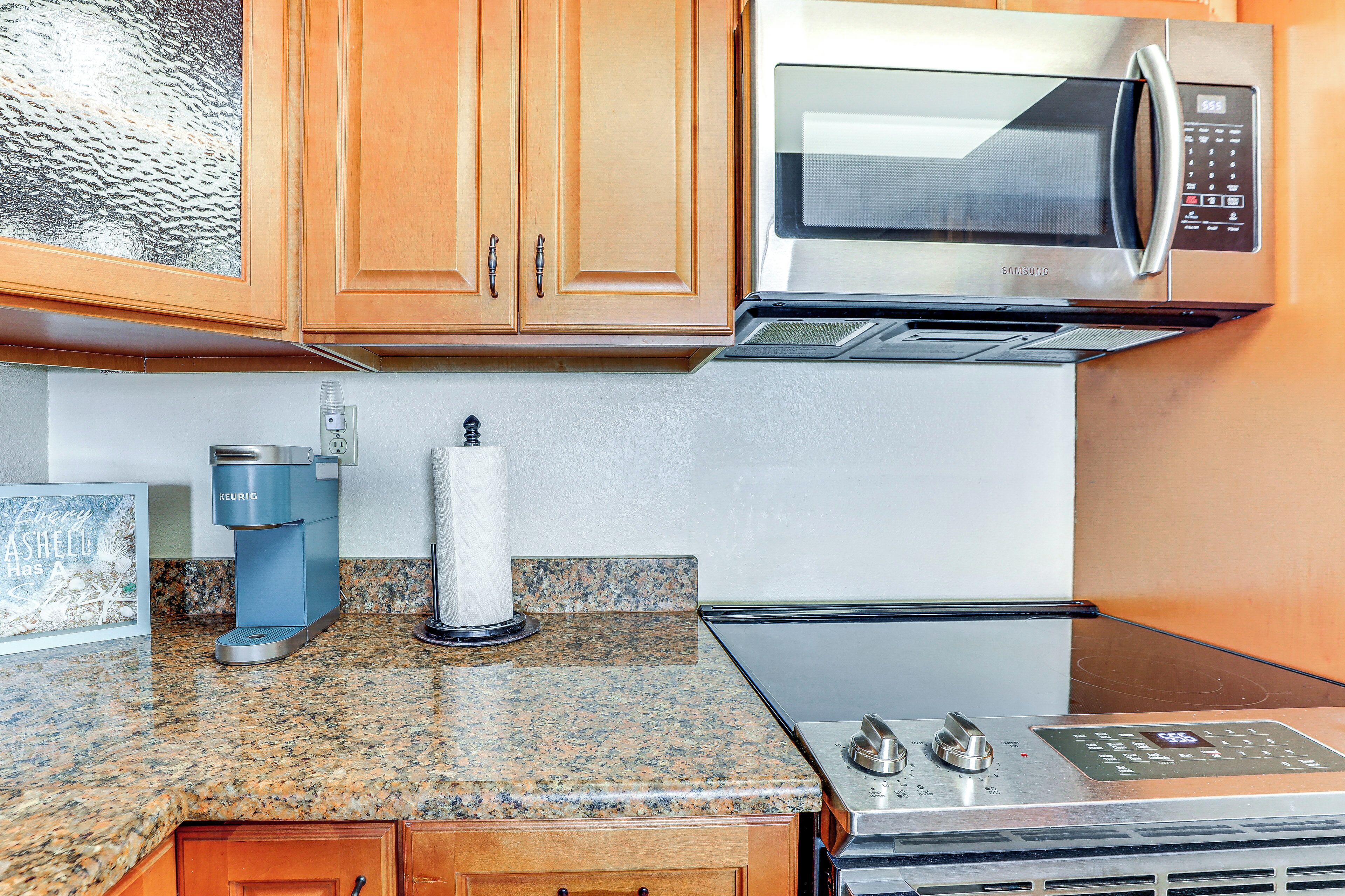 A kitchen with wooden cabinets, a stainless steel microwave, a Keurig coffee maker, and a granite countertop.
