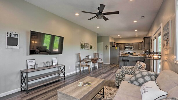 A modern living room with a sofa, coffee table, and TV. There is a dining area with chairs and a table, and a kitchen in the background. - Lake Views, Fire Pit! Blue Cabin Ozarks Getaway (Camdenton)