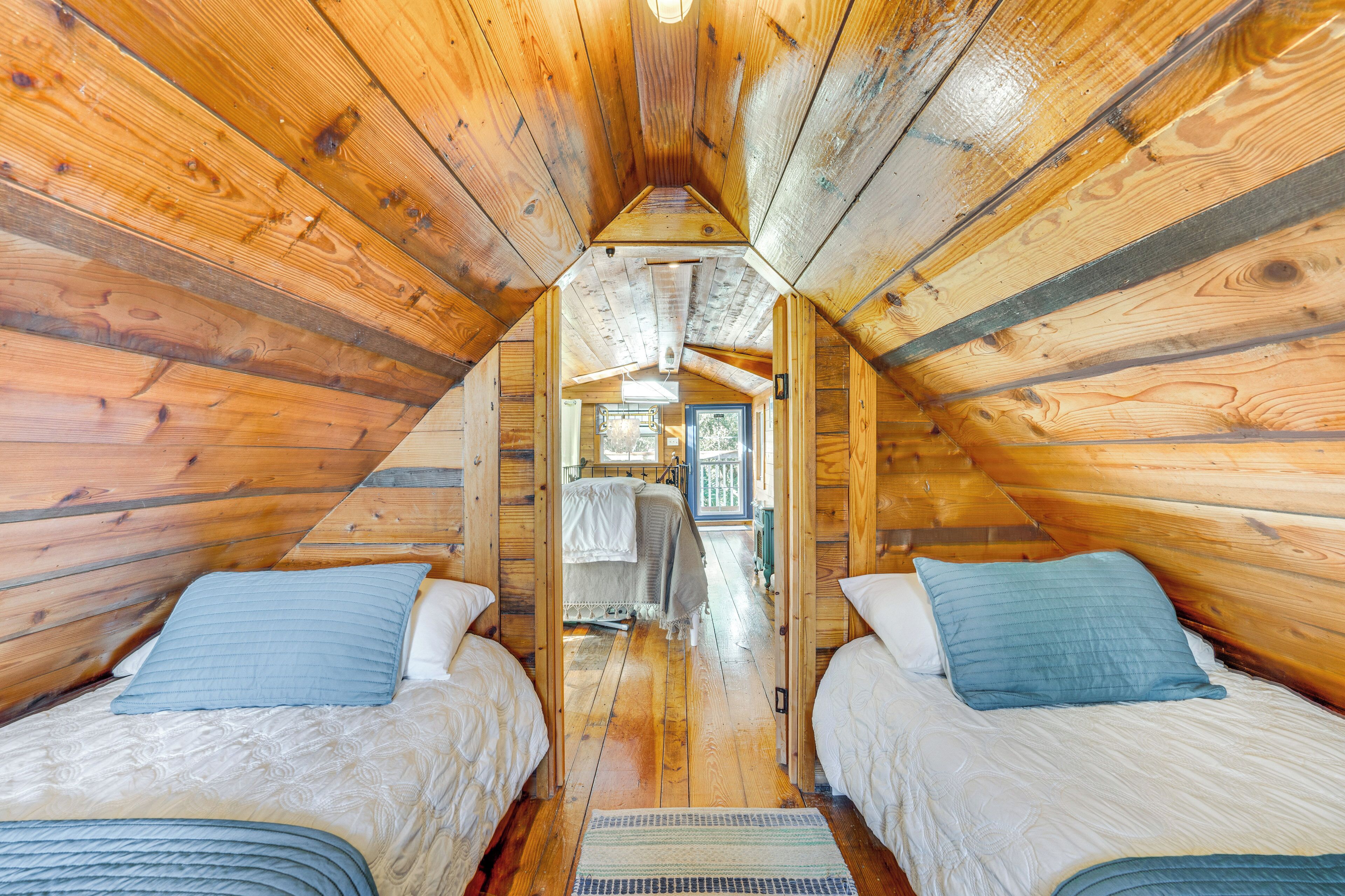 A cozy attic bedroom with wooden walls and a sloped ceiling, featuring two beds with blue pillows and a central walkway.