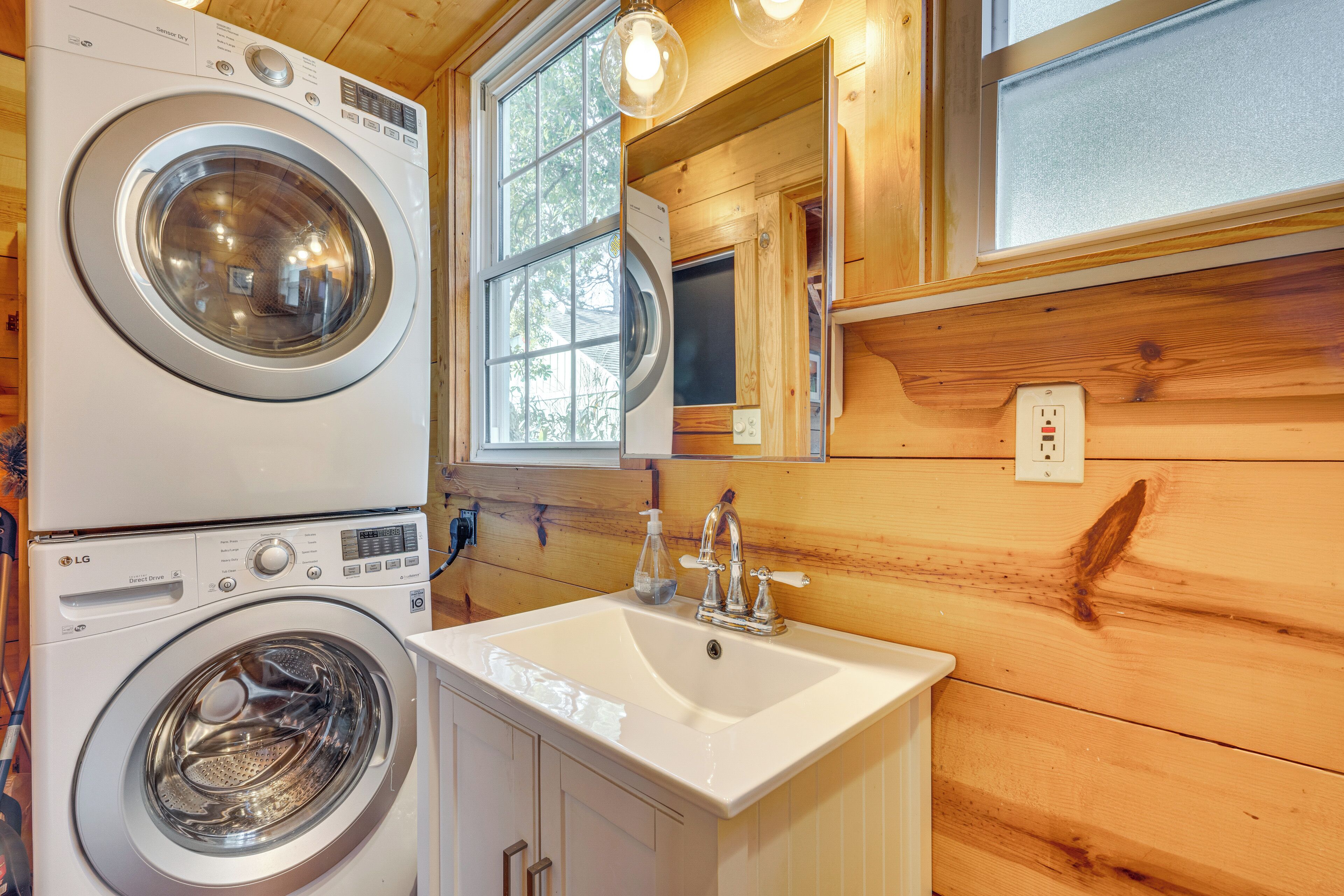 A compact laundry room with a front-loading washer and dryer, a sink with a faucet, and wooden walls.