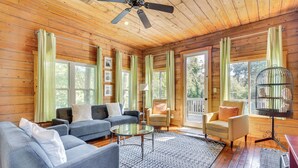A cozy cabin interior with a wooden ceiling, a ceiling fan, a blue sofa, a round coffee table, and a birdcage.