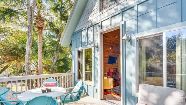 A covered outdoor deck with a table and chairs, a sofa, and a view of the interior through a glass door.