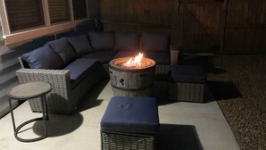 Une terrasse avec un foyer, des meubles en osier et une vue sur la maison.