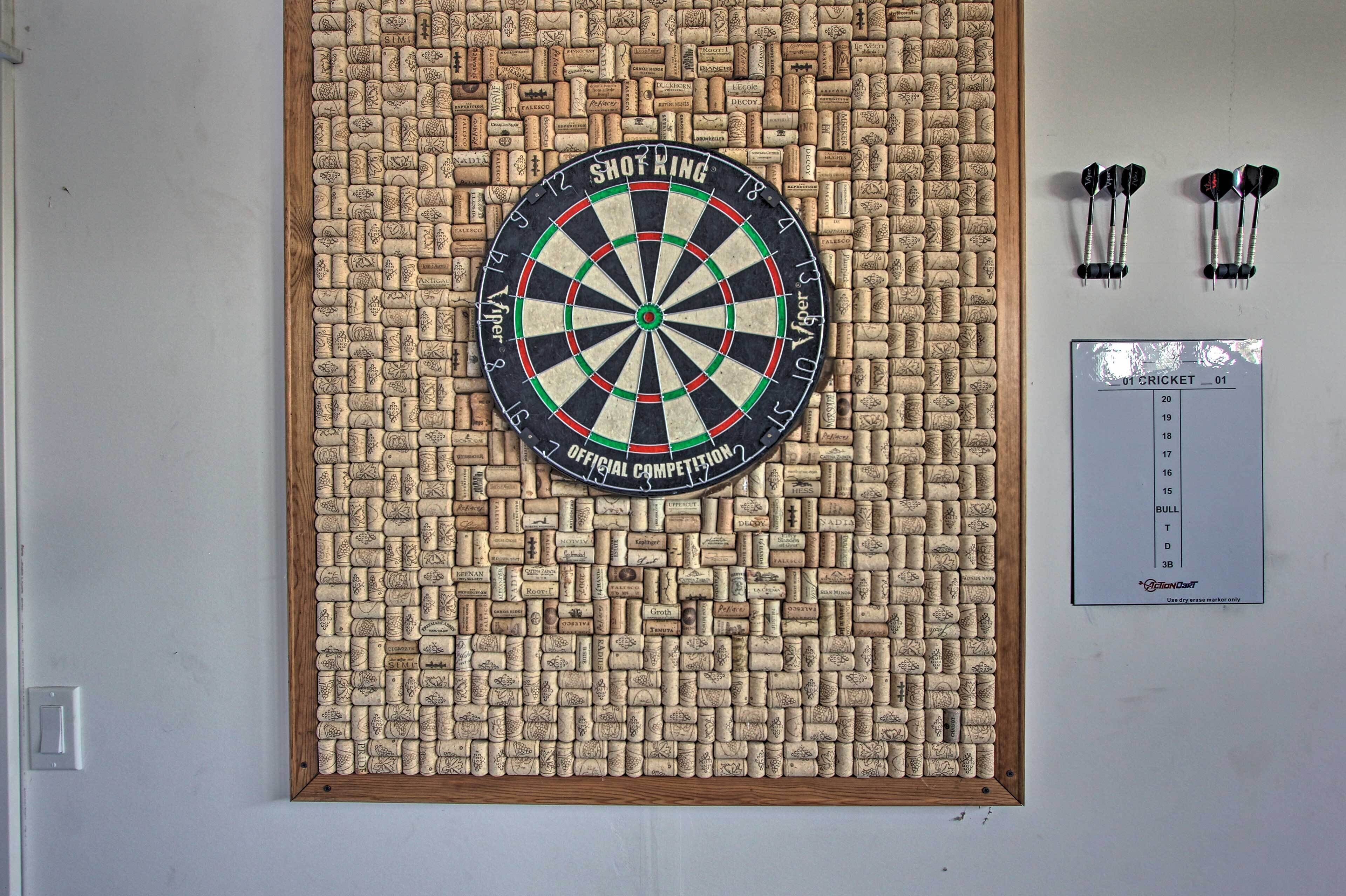 A dartboard mounted on a corkboard wall with a scorecard and darts beside it.