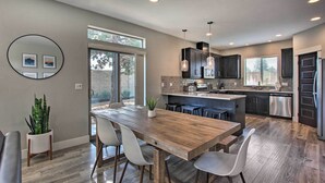 Une cuisine moderne avec des meubles de rangement de couleur sombre, une table à manger en bois et une grande fenêtre.