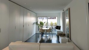 A modern living room with a sofa, a dining area with chairs and a table, and a large window with plants. - Atico-loft Mompó. Lujo Marítimo (València)